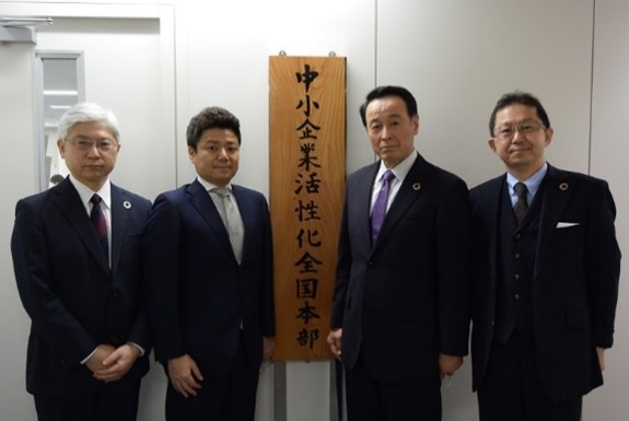 萩生田光一経済産業相が揮毫（きごう）した全国本部の看板を前に豊永厚志理事長（右から2人目）ら